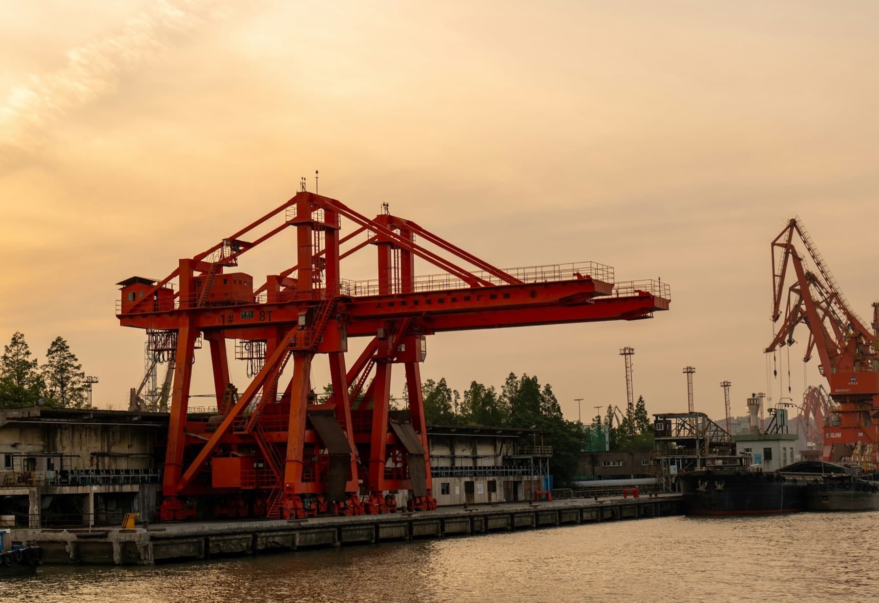 A red steel gantry crane on a river wharf at golden hour